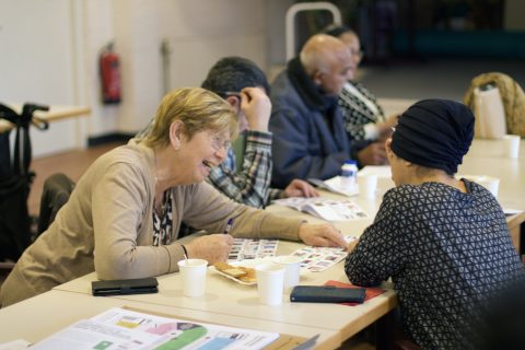 Enkele mensen volgen een workshop Hulp bij bankzaken. Ze zitten aan een tafel met boekjes voor zich en praten daarover.