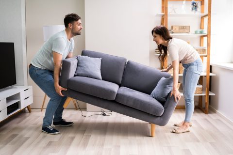 Man en vrouw tillen samen een bank op in de huiskamer.