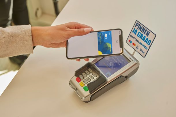 Een vrouw betaalt contactloos met haar mobiel. Een bordje "pinnen ja graag" is te zien op het pinapparaat.